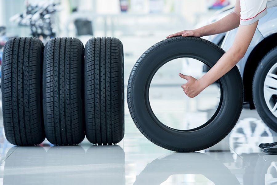 A person gives a thumbs up through a tire with three tires standing nearby, waiting to be installed on a car.